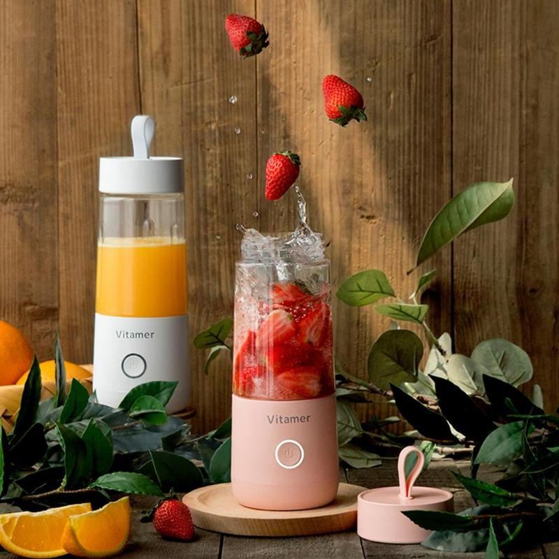 Vitamer rechargeable personal blender with one bottle of juice and another blending fresh strawberries surrounded by fruits and leaves